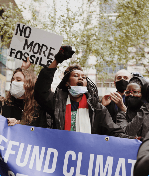 Climate protest with people holding signs including 'NO MORE FOSSILS' and 'FUND CLIMATE'